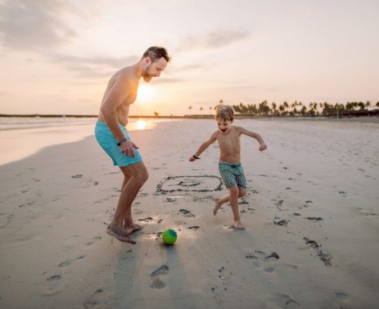 Father with his son plaing football on the beach.