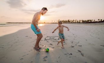Father with his son plaing football on the beach.