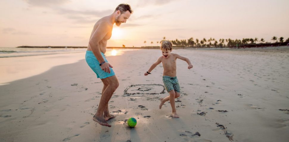 Father with his son plaing football on the beach.